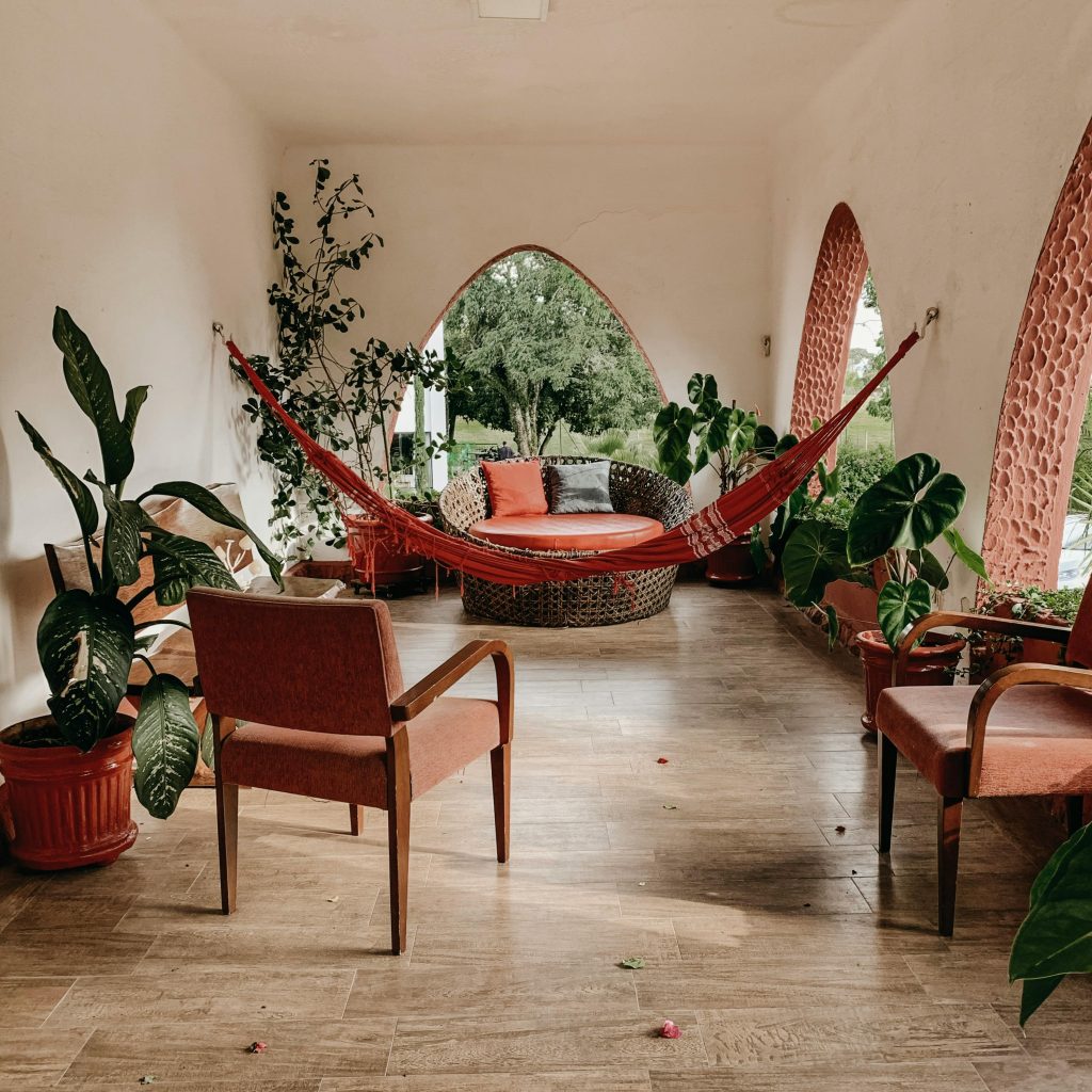 Serene indoor patio featuring a hammock, lush green plants, and comfortable seating for relaxation.